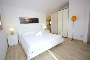 A hotel room with a bed, a nightstand with a lamp, a painting on the wall, and a wardrobe.