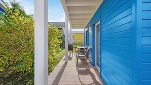 A covered outdoor area with a wooden deck, a table and chairs, and a blue building. - Pet friendly home in Süssau/Ostsee with sauna (Süssau/Ostsee)