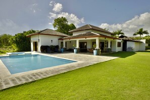 A two-story house with a swimming pool, a covered patio, and a well-maintained lawn.