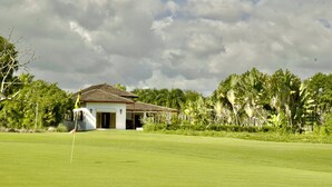Een golfbaan met een clubhuis, omringd door weelderige begroeiing en palmbomen.