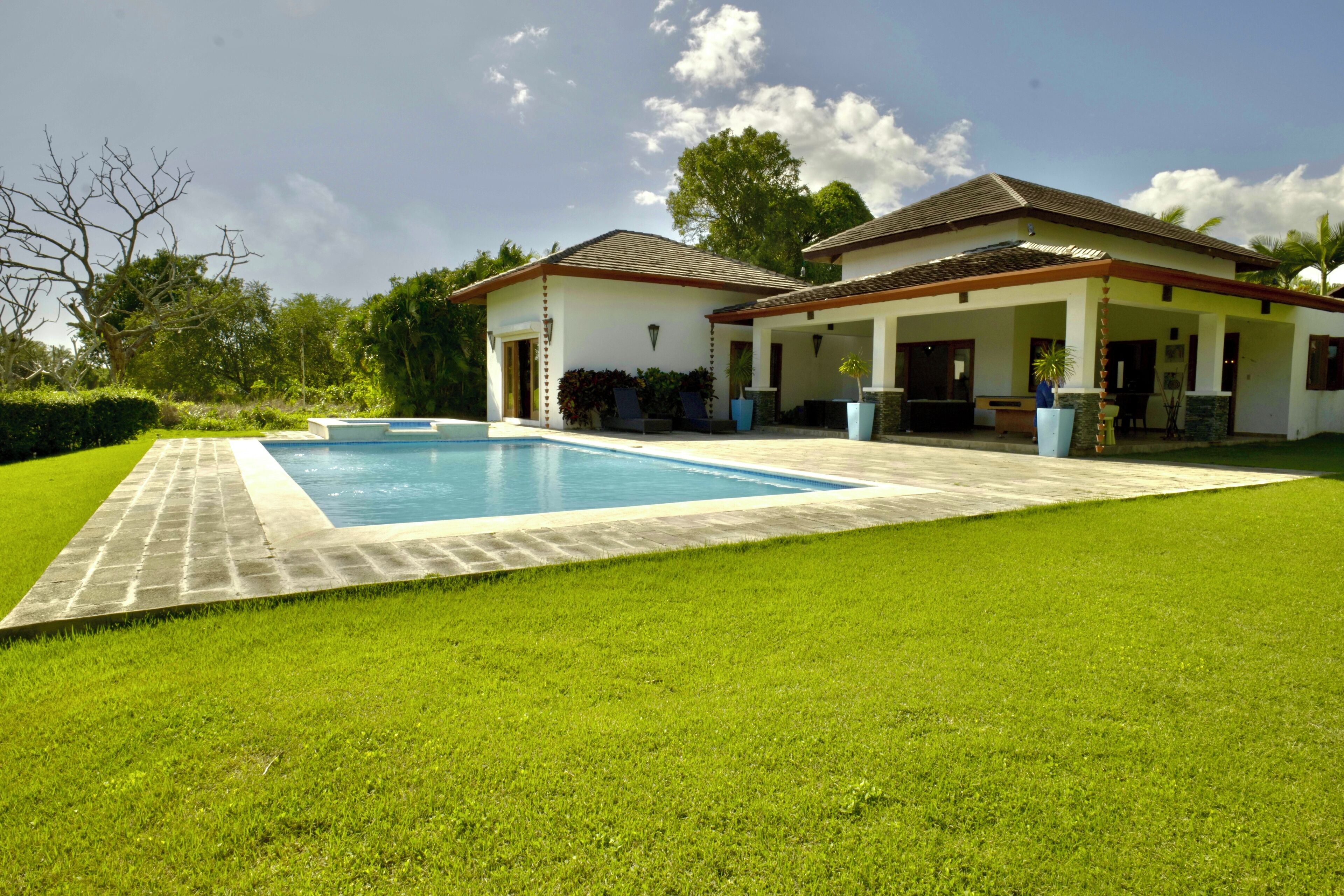 A house with a swimming pool, a covered patio, and a well-maintained lawn.