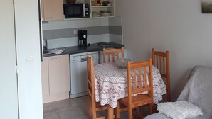 A compact kitchen with a microwave, coffee maker, and a small cabinet. There is a dining table with chairs and a white sofa in the living area. - Maison et Loisirs (Calvisson)