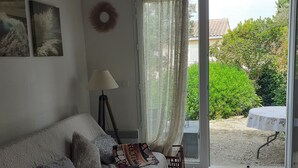 A living room with a sofa, a coffee table, and a view of a garden through a glass door. - Maison et Loisirs (Calvisson)