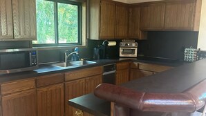A kitchen with wooden cabinets, a microwave, an oven, and a bar area with a cushioned stool. - The Sequim Tree House is a spacious one bedroom with a bonus room for more guest (Sequim)
