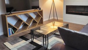 Ein modernes Wohnzimmer mit einem großen Flachbildfernseher auf einer Holzkonsole, einer Stehlampe, einem Kamin und einem Sofa.