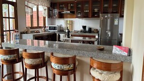 A kitchen with granite countertops, wooden stools, a refrigerator, a microwave, and a coffee maker. - Casa Oxapampa (Oxapampa)