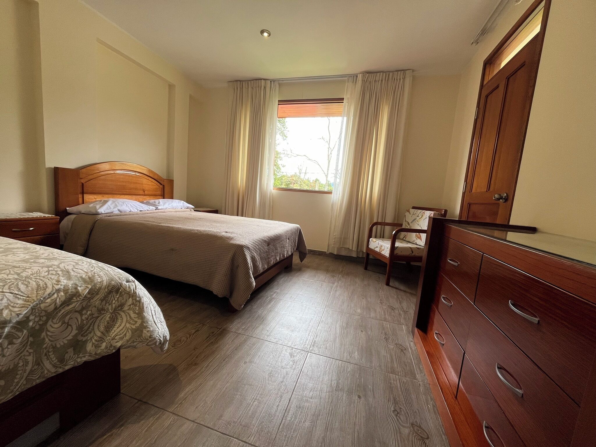Une chambre avec deux lits, une commode en bois, une chaise et une fenêtre avec des rideaux.