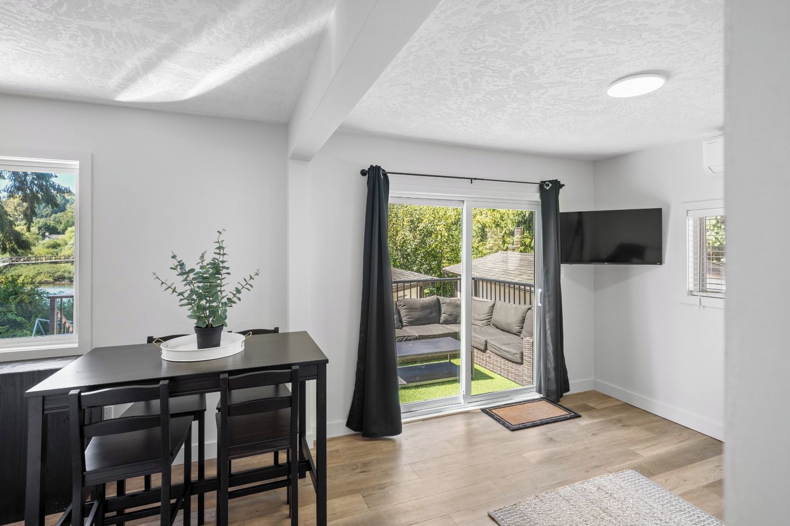 A modern room with a dining table, chairs, a potted plant, a sliding glass door to an outdoor area, and a mounted TV.