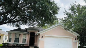 Une maison à deux étages avec un garage, un porche à l’avant et un grand arbre devant.