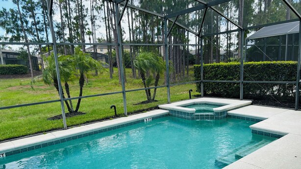 Une piscine dotée d’une enceinte en verre, entourée d’une pelouse et d’arbres.