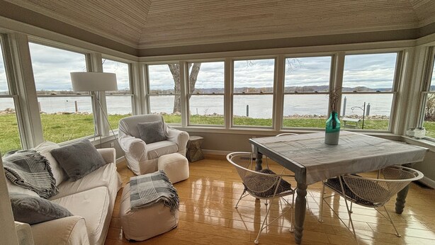 A sunroom with a wooden ceiling, large windows, a white table, and a white sofa with cushions.