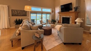 A spacious living room with a fireplace, large windows, and a flat-screen TV.