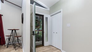A room with a wooden floor, a sliding glass door leading outside, a white door, and a small table with stools. - Becca's Place - Near LeConte + Ripken | Pet-Friendly w/ Hot Tub & Games (Pigeon Forge)
