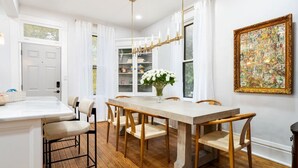 A dining area with a wooden table and chairs, a vase of white flowers, and a large framed picture on the wall. - Luxury Rose Manor - Perfect for Bachelorettes! (Columbus)