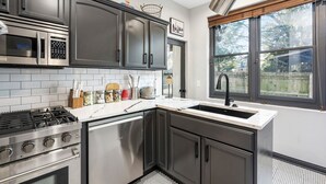 A modern kitchen with stainless steel appliances, dark cabinetry, and a large window providing natural light. - Short North Clubhouse w/Hot Tub! Free Parking! (Columbus)