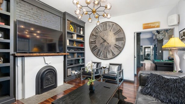 A modern living room with a large wall clock, a fireplace, and a television. - Short North Clubhouse w/Hot Tub! Free Parking! (Columbus)