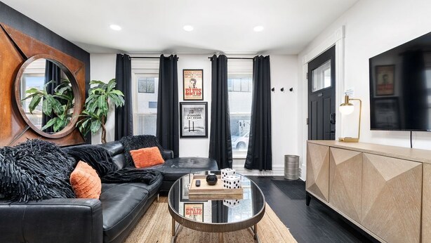 Een moderne woonkamer met een zwarte leren bank, een glazen salontafel en een houten kast.