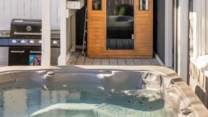 Een hottub in een overdekte buitenruimte, met een houten deur en een barbecue in de buurt.