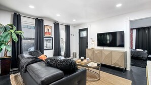 Een moderne woonkamer met een zwarte leren bank, een flatscreen televisie en een minimalistische kast.