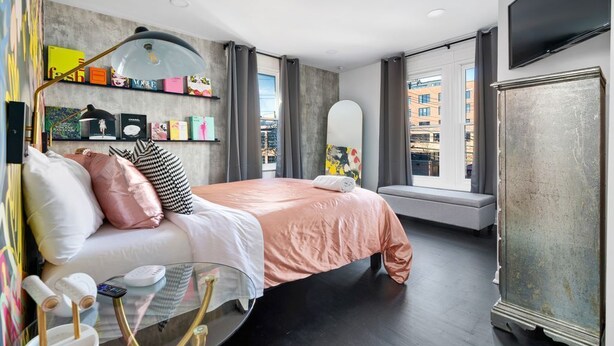 Habitación de hotel moderna con cama, mesita de noche, lámpara y un ventanal con vistas a la ciudad.