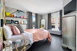Ein modernes Hotelzimmer mit Bett, Nachttisch, Lampe und einem großen Fenster mit Blick auf die Stadt.