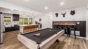 Um espaço de estar moderno com mesa de bilhar, cozinha e bar.