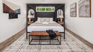 Um quarto moderno com uma cama, mesas de cabeceira, um banco, um ventilador de teto e obras de arte nas paredes.