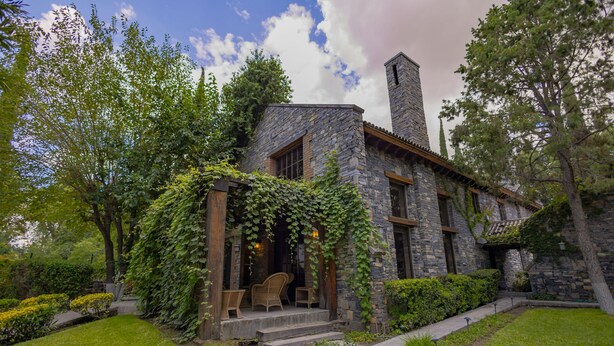 Una casa de pedra amb un porxo cobert, escales cap a l'entrada i una petita zona d'seients a l'exterior.