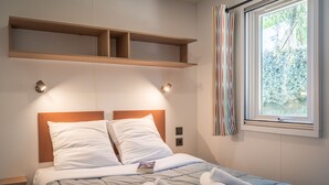 Una cama bien hecha con cabecera, dos mesitas de noche y una ventana con cortinas.