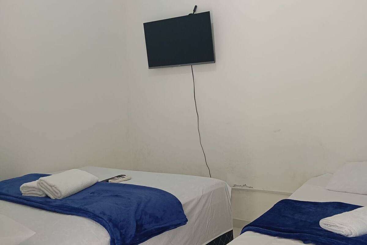 Een hotelkamer met twee bedden, elk met een blauwe deken en een wit kussen. Een flatscreen televisie is aan de muur tussen de bedden bevestigd.