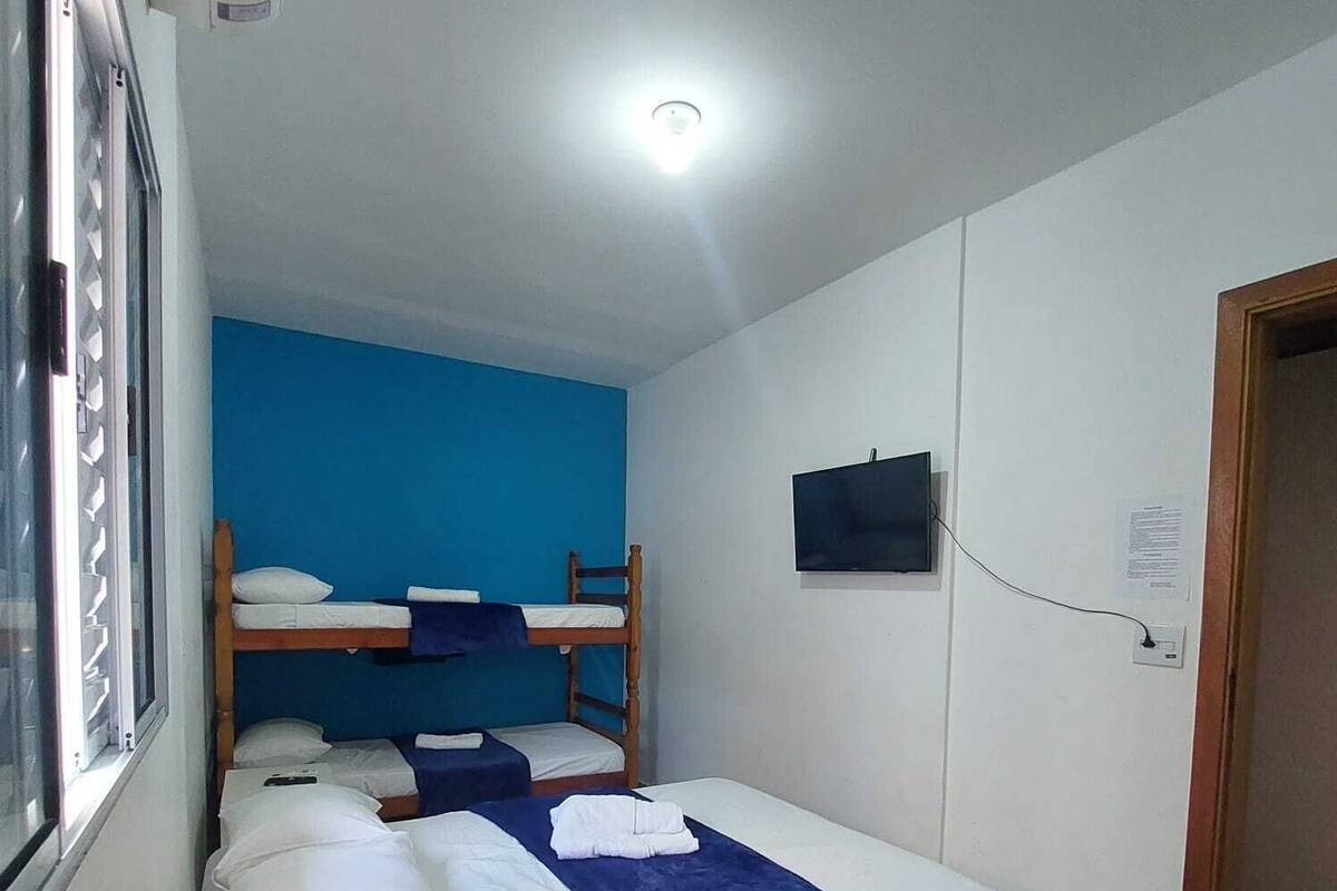 Een slaapzaal met stapelbedden, een aan de muur bevestigde televisie en een raam aan de linkerkant.