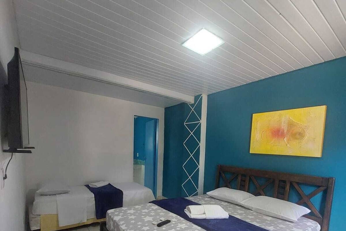 Een hotelkamer met een groot bed, een kleiner bed, een televisie en een blauwe muur met een geel schilderij.