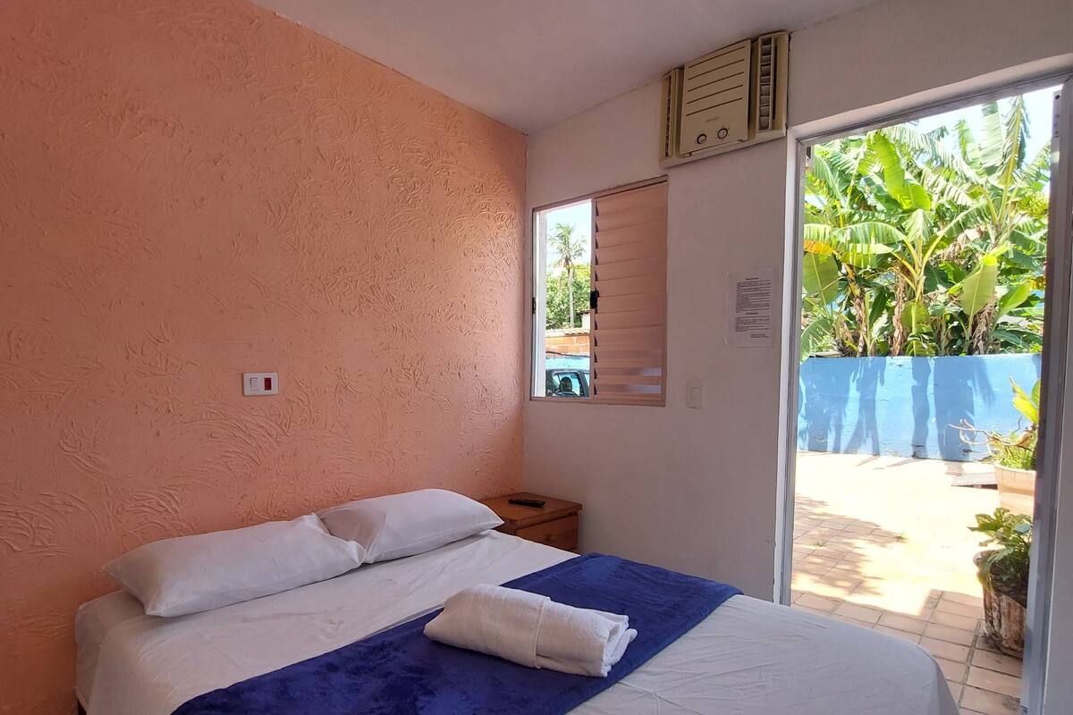 Een slaapkamer met een bed, nachtkastje, raam en uitzicht.