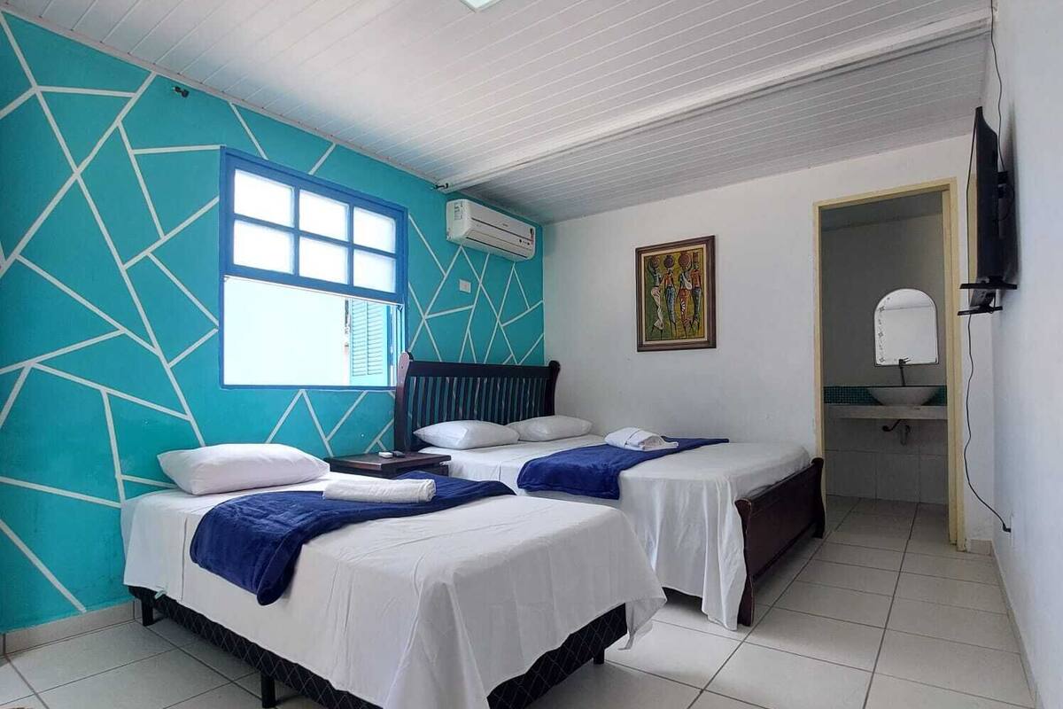 Een hotelkamer met twee bedden, een raam, een airconditioning, een schilderij en een televisie.