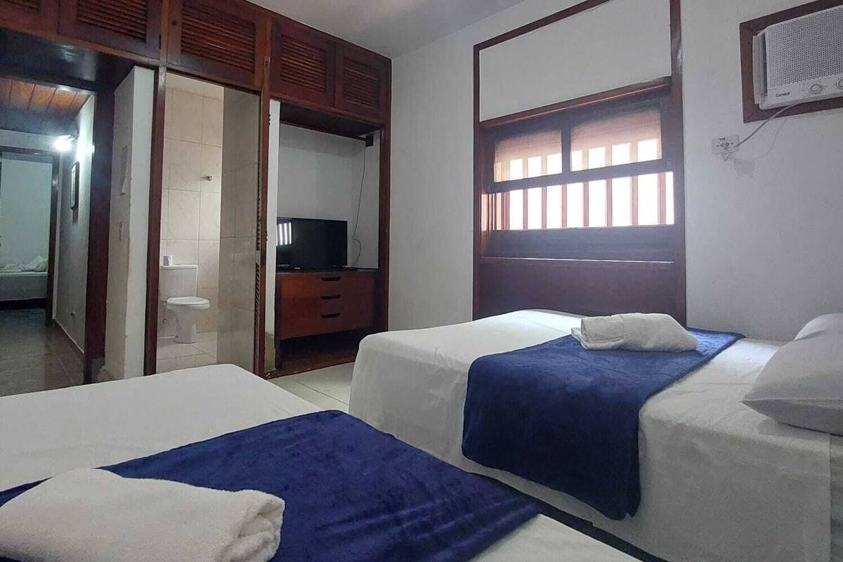 Een hotelkamer met twee bedden, een kledingkast, een televisie en een raam met jaloezieën.