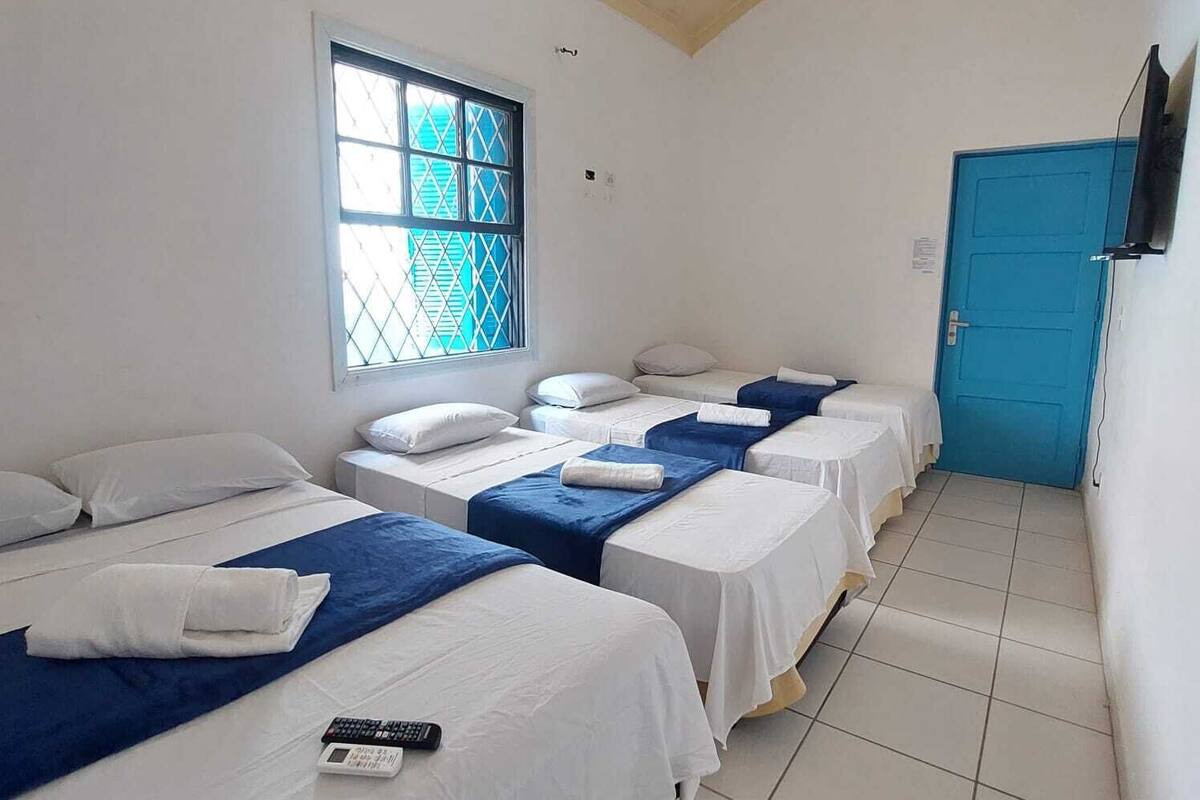 Een hotelkamer met drie eenpersoonsbedden, een raam met uitzicht, een blauwe deur en een aan de muur bevestigde televisie.