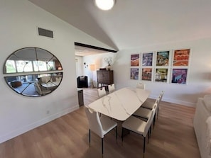 A modern dining area with a marble table, white chairs, a round mirror, and a wall with framed pictures.