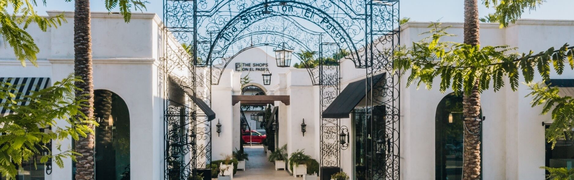 Un bâtiment blanc avec une grille en fer forgé et une enseigne indiquant : « Les boutiques d’El Paseo ».