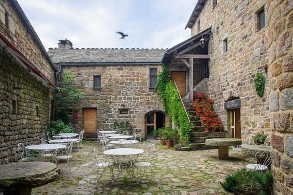 A stone courtyard with outdoor seating and a staircase leading to a wooden door. - Auberge La Régordane (Prevencheres)