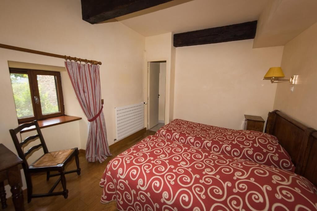 A bedroom with a bed, a chair, a window with curtains, and a lamp.