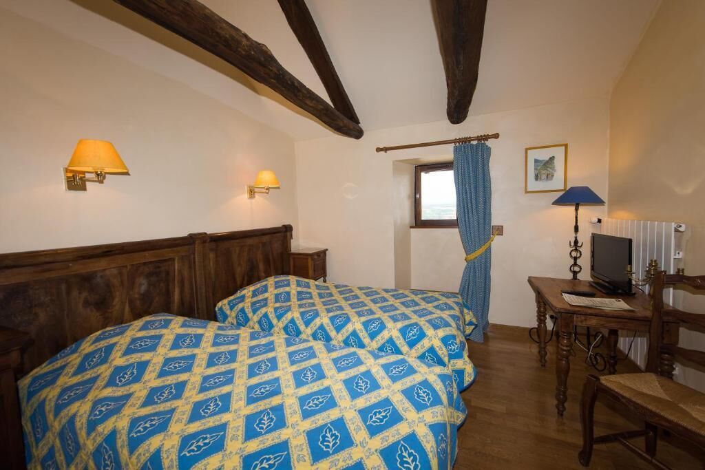 Une chambre avec deux lits, des têtes de lit en bois, une petite table avec une lampe et une fenêtre avec des rideaux.