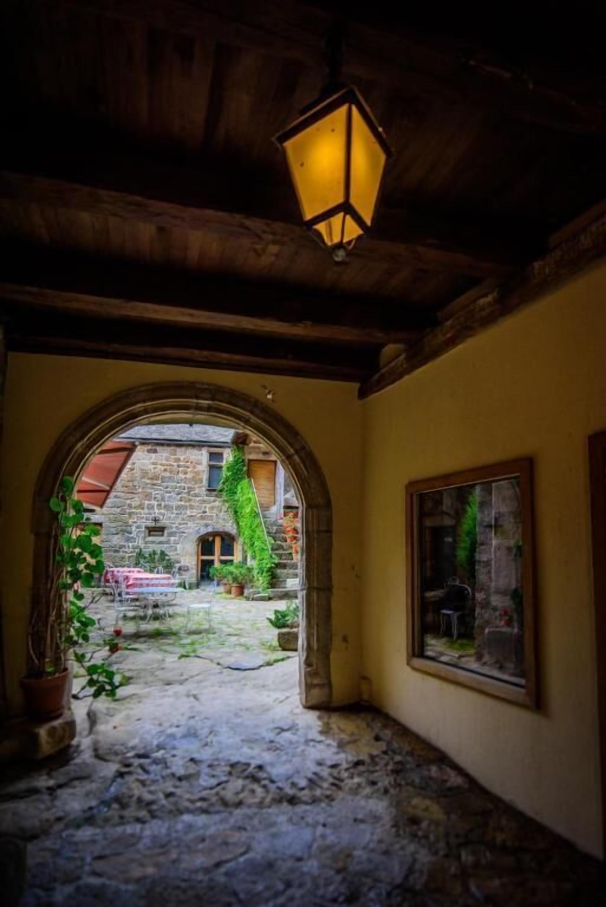 Un pasillo de piedra con un arco que da a un espacio exterior con plantas y un edificio.