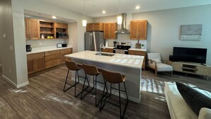 Une cuisine moderne dotée de meubles en bois, d’appareils électroménagers en acier inoxydable et d’un îlot central agrémenté de tabourets de bar.