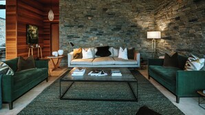 Ein modernes Wohnzimmer mit einer Steinwand, grünen Sofas und einem Couchtisch mit Büchern.