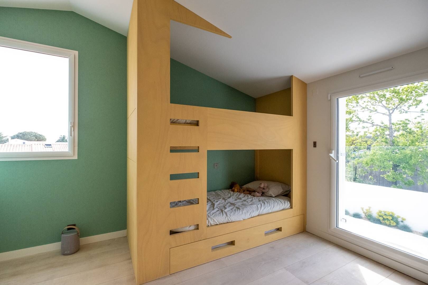 A bunk bed with a wooden ladder, a window, and a view of greenery outside.