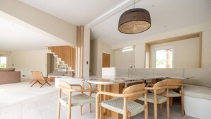 A modern dining area with a round table and six wooden chairs, a staircase with wooden railings, and a large woven pendant light.