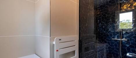 Un baño moderno con un banco blanco, cabina de ducha de vidrio y pared de mosaico negro.