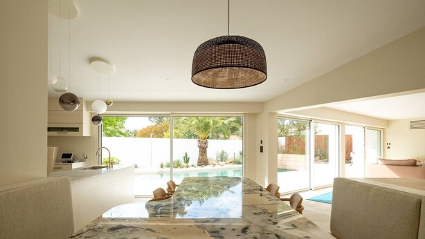 A spacious living area with a large glass table, a woven pendant light, and a view of a swimming pool.