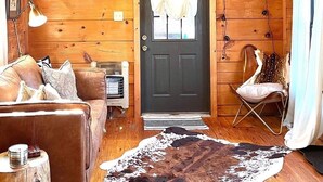 L’intérieur d’un chalet accueillant, avec une porte en bois, un canapé en cuir, un tapis en peau de vache et un petit fauteuil.