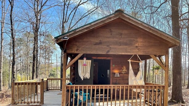 Une cabane en bois avec une véranda, une porte et un hamac suspendu.
